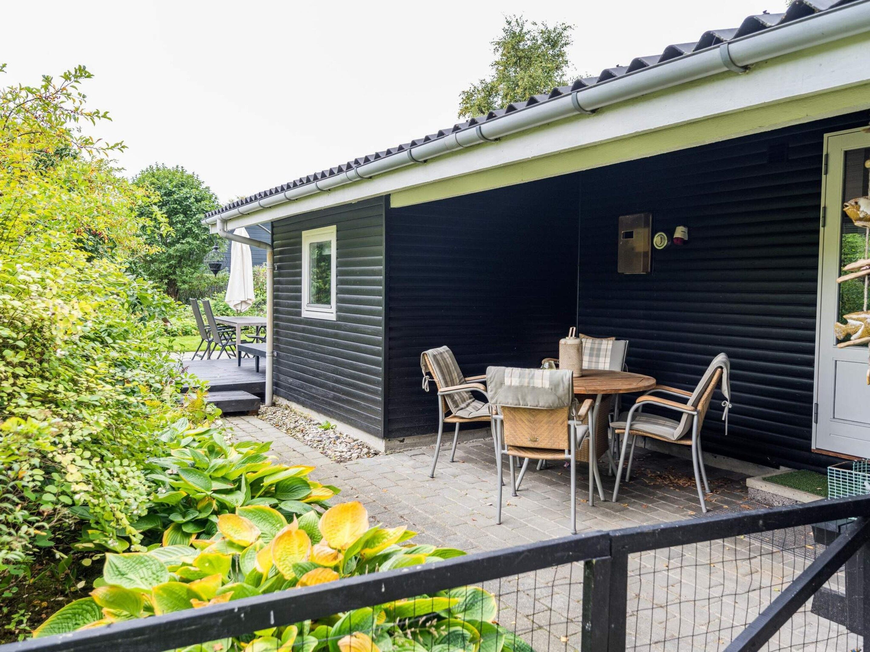 Een klein, donker gebouw met een terras, compleet met een ronde tafel en stoelen.