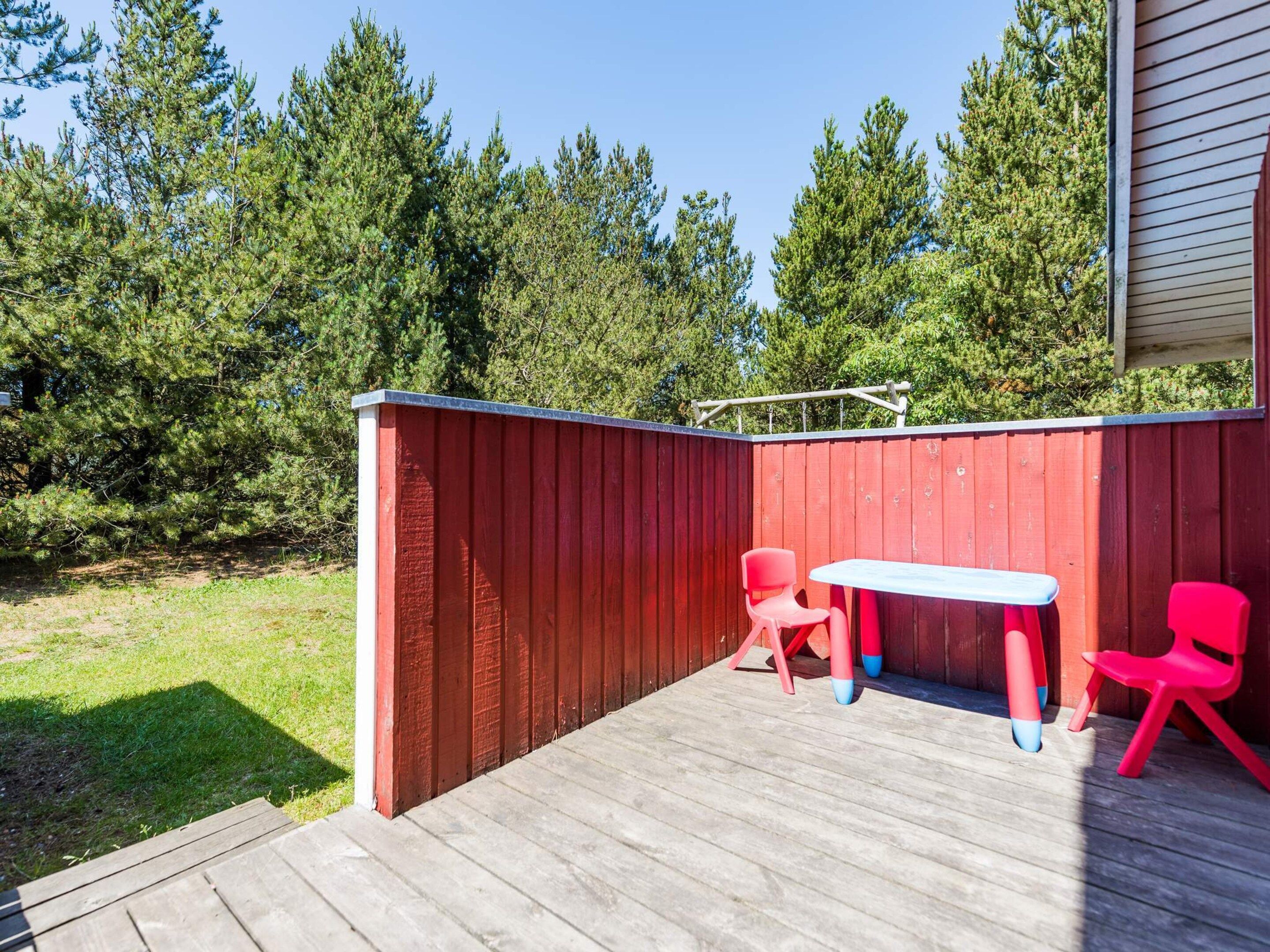 A wooden deck with a red fence, two red chairs, and a small table.