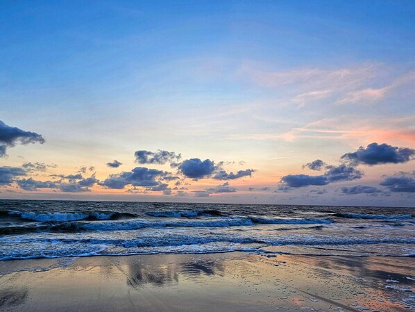 A beach with waves, a clear sky, and clouds.