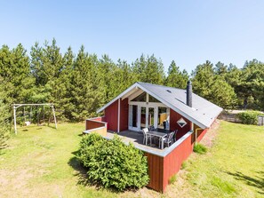 Une cabane en bois rouge avec un patio, entourée d’une cour verdoyante et d’arbres touffus.