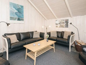 Une pièce comprenant deux canapés en cuir noir, une table basse en bois et un mur orné d’un tableau encadré et d’une enseigne.