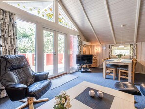 A spacious living area with a leather sofa, a dining table with chairs, a flat-screen TV, and a large window with a view of the outdoors.