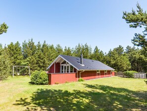 Une cabane en bois rouge, avec un toit en pente, entourée d’une cour verdoyante et d’arbres touffus.