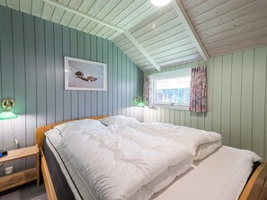 Une chambre à coucher avec un lit double, une table de chevet avec une lampe, une fenêtre avec des rideaux et un tableau encadré au mur.
