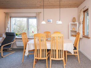 A dining area with a table set for four, wooden chairs, a sofa, and a window with curtains.