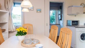 A dining area with a table set for two, a washing machine, and a microwave in the adjacent kitchen. - 5 Person Holiday Home in Norre Nebel (Norre Nebel)