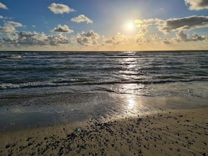 A beach with waves, a clear sky, and the sun setting or rising.