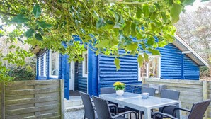 A blue log cabin with a patio area, a table, and four chairs. - 5 Person Holiday Home in Norre Nebel (Norre Nebel)