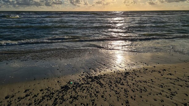 A beach with waves, a clear sky, and the sun setting or rising. - 5 Person Holiday Home in Norre Nebel (Norre Nebel)