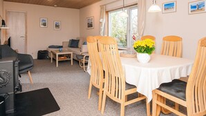 A cozy room with a dining table, wooden chairs, a sofa, and a fireplace. - 5 Person Holiday Home in Norre Nebel (Norre Nebel)