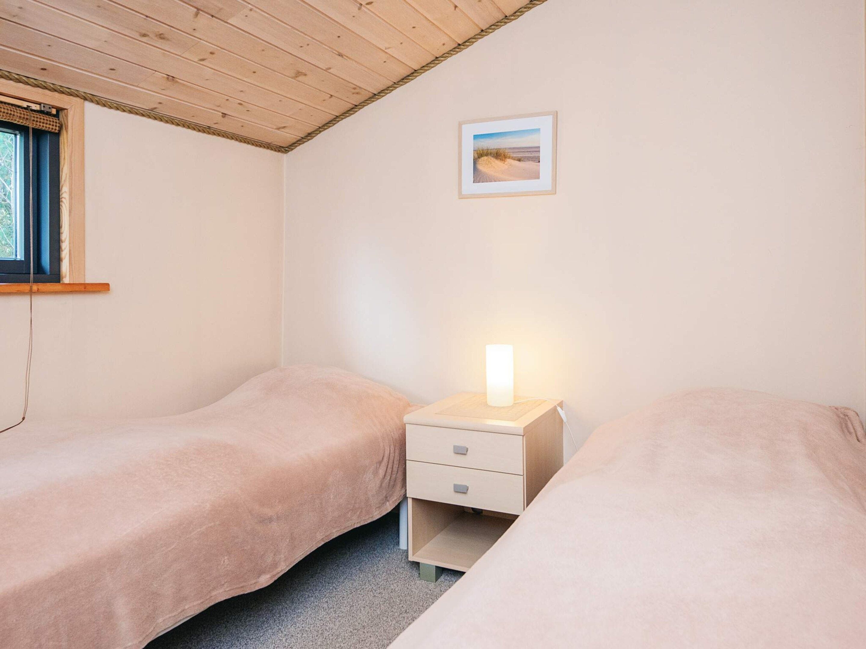 A bedroom with two single beds, a bedside table with a lamp, a window, and a framed picture on the wall.