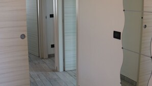A hallway with a wooden floor, a door with a circular handle, and a wall-mounted light fixture. - Holiday Apartment near Lake, Shared Swimming Pool (Lazise)