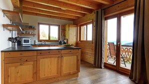Une cuisine spacieuse dotée de meubles en bois, d’un four à micro-ondes et d’un grand îlot central. Une porte-fenêtre coulissante donne accès à un balcon offrant une vue sur l’extérieur.