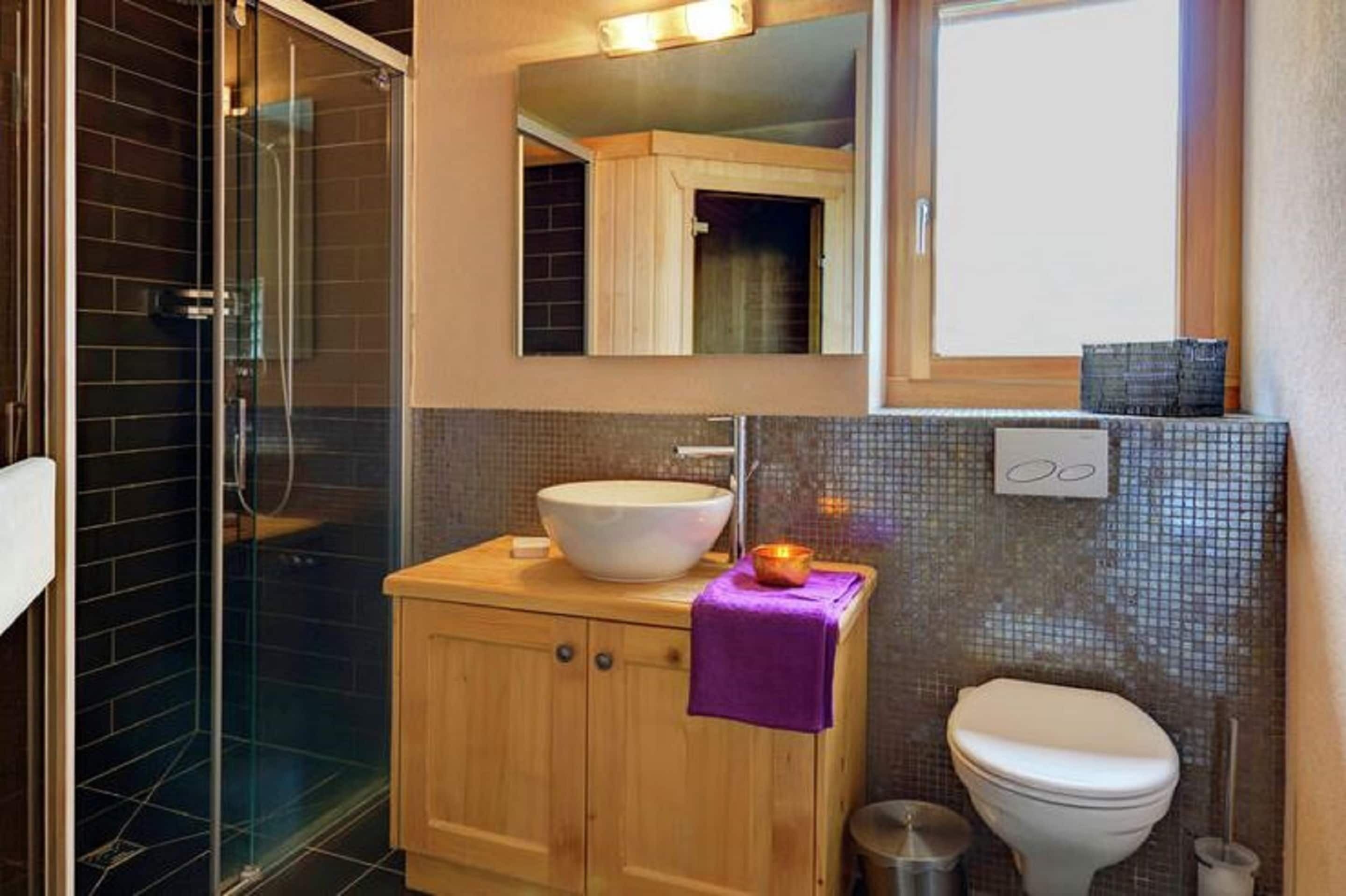 A bathroom with a glass shower enclosure, a wooden vanity with a white sink, and a white toilet.