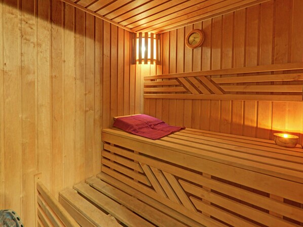 A sauna with wooden walls and benches, a clock, and a small table with a candle.