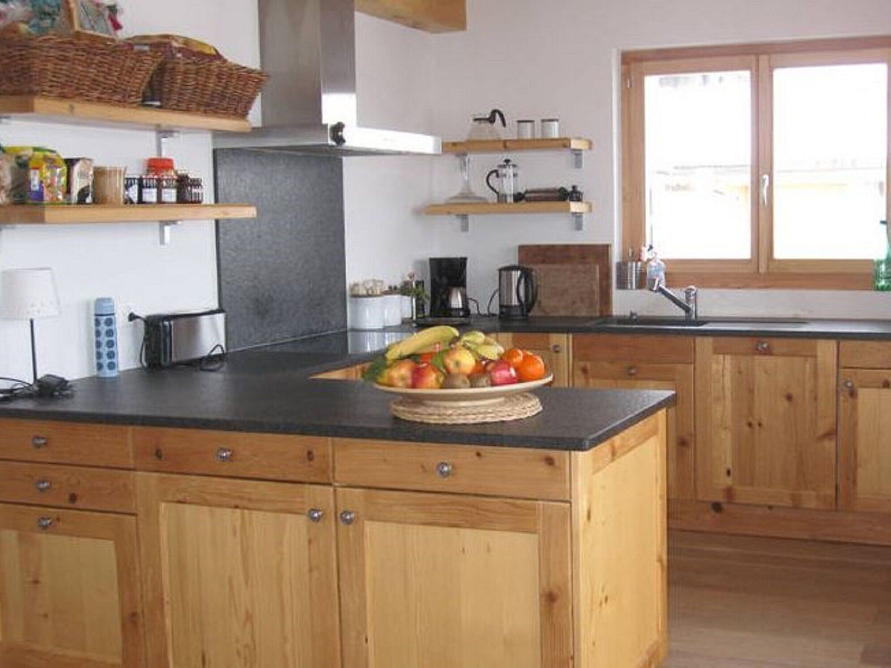 A kitchen with wooden cabinets, a central island with a fruit bowl, and a window with a view.