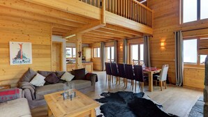 Une cabane en bois spacieuse comprenant un coin repas, un ensemble de canapés et un tapis en peau de vache.
