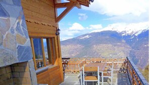 Une cabane en bois aux murs de pierre, dotée d’un balcon offrant une vue sur un paysage montagneux.
