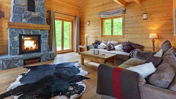 L’intérieur chaleureux d’un chalet avec une cheminée en pierre, des murs en bois, un canapé et une table à manger.