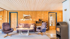 A cozy room with wooden walls, a sofa, two armchairs, a coffee table, and a fireplace. - 6 Person Holiday Home in Norre Nebel (Norre Nebel)