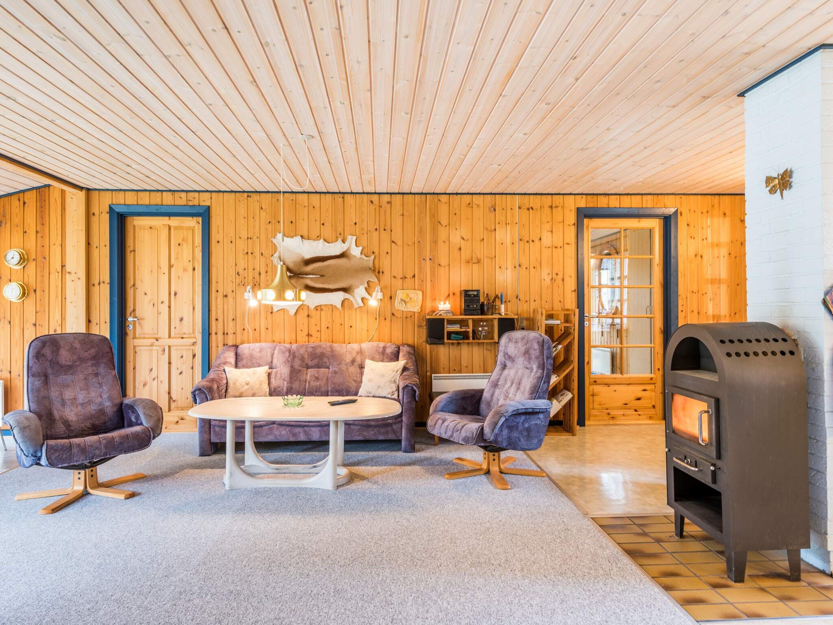 A cozy room with wooden walls, a sofa, two armchairs, a coffee table, a fireplace, and a wooden ceiling.