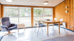 A room with a wooden ceiling, large windows, a round table, and a grey upholstered chair. - 6 Person Holiday Home in Norre Nebel (Norre Nebel)