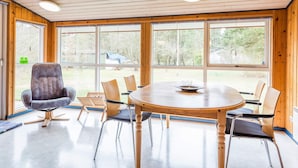 A spacious room with a round wooden table and chairs, large windows, and a wooden ceiling. - 6 Person Holiday Home in Norre Nebel (Norre Nebel)