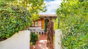 Un sendero en un jardín conduce a un patio con mesa y sillas, rodeado de abundante vegetación.