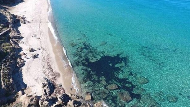 Vista aérea de una playa con aguas turquesas cristalinas y formaciones rocosas cerca de la orilla.