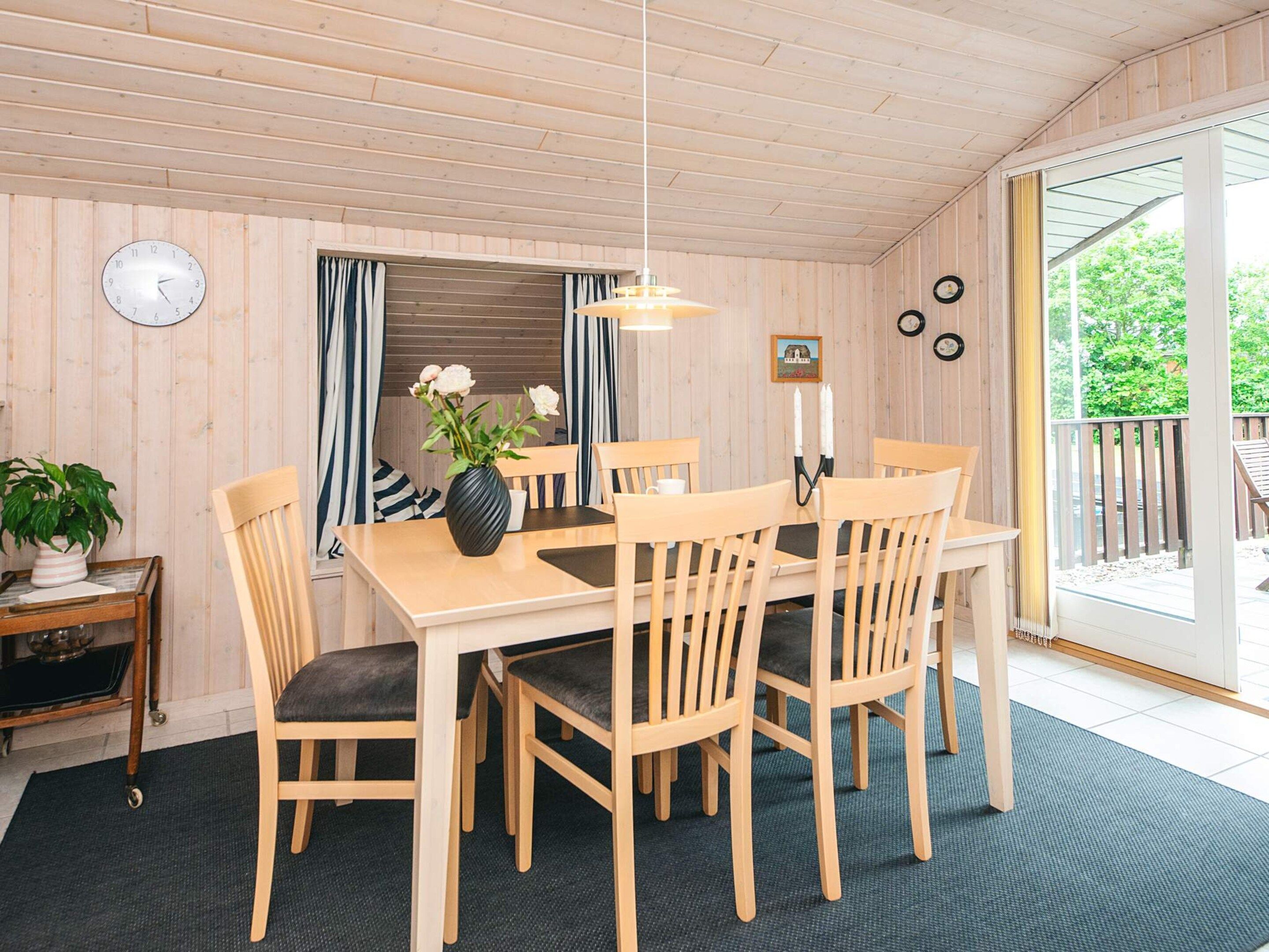 A wooden-paneled room with a dining table, chairs, a clock, and a window with curtains.