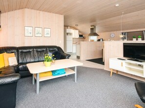 Un salon moderne avec un canapé en cuir noir, une table basse blanche et un téléviseur posé sur un meuble blanc.