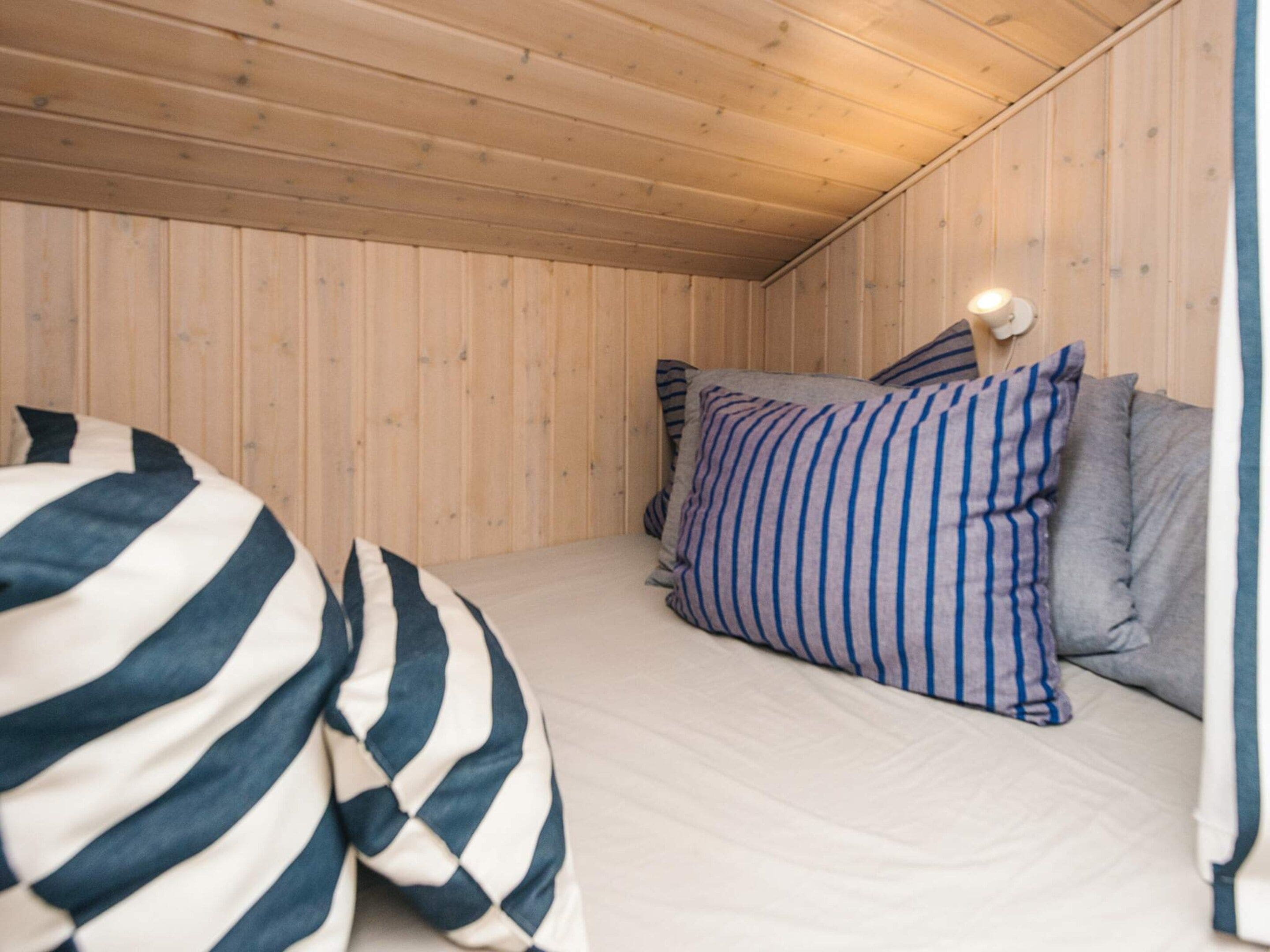 A room with a bed, striped pillows, and a wooden ceiling.