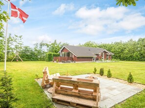 Une maison avec une terrasse, une balançoire et un foyer extérieur dans le jardin.