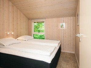 A bedroom with a bed, a window, a door, and a wall-mounted light fixture.