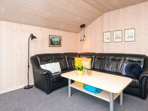 A room with a black leather sofa, a small table with a vase, a floor lamp, and framed artwork on the wall.