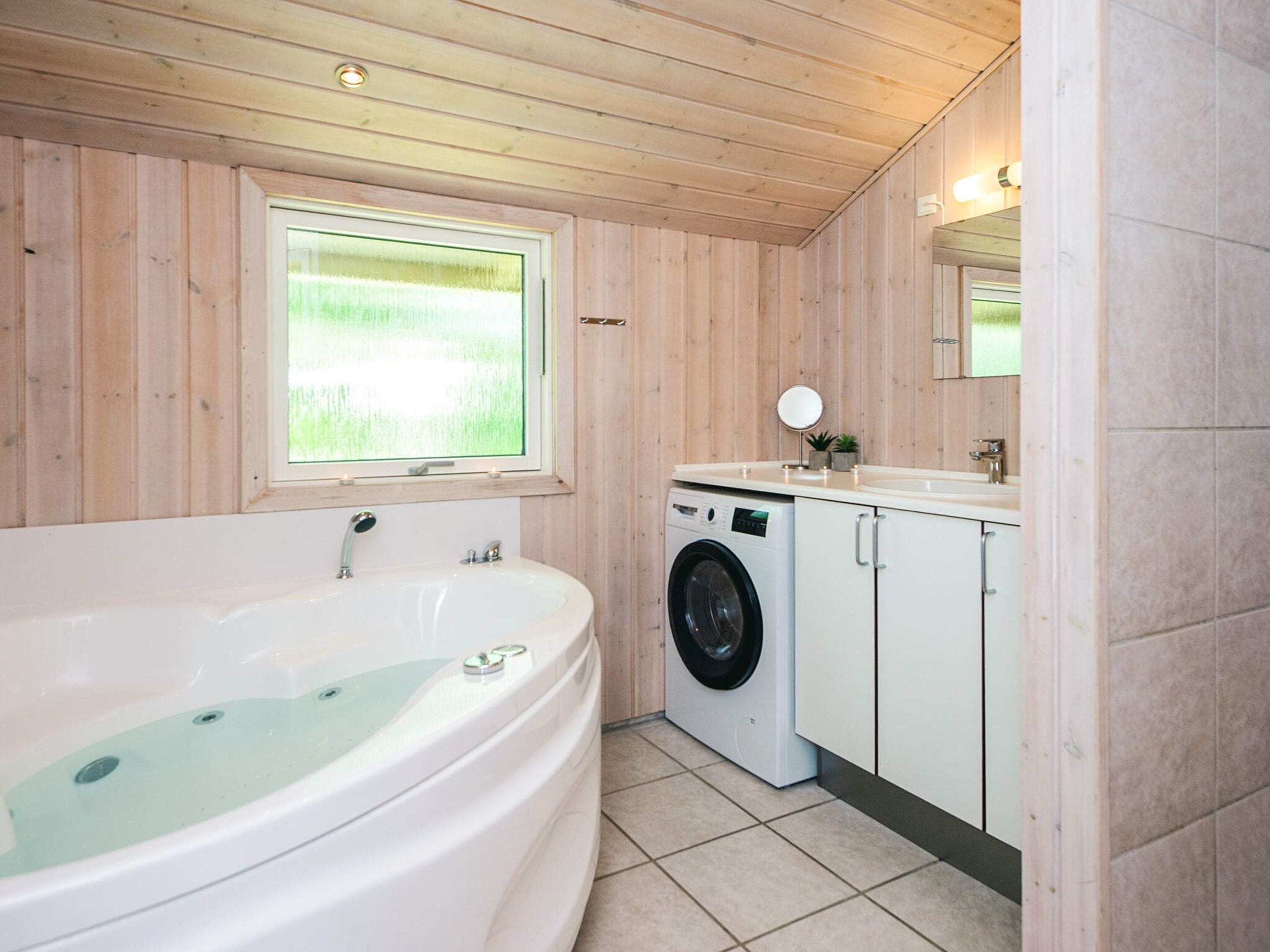 A bathroom with a bathtub, a washing machine, and a sink.