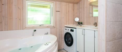 A bathroom with a bathtub, a washing machine, and a sink.