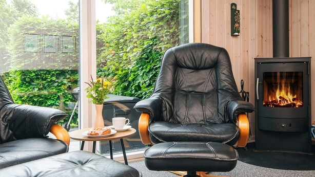 A cozy room with a leather sofa, a leather armchair, a small table with a cup and a pastry, and a wood-burning stove. - 6 Person Holiday Home in Tarm (Tarm)