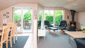 A cozy room with a wooden ceiling, a fireplace, a dining area with chairs, and a large window offering a view of greenery. - 6 Person Holiday Home in Tarm (Tarm)