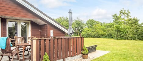 A wooden deck with outdoor furniture, a chimney, and a grassy yard.
