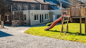 A stone building with a gravel driveway, a wooden play structure, and a grassy area. - Timeless Cottage in Vresse-sur-semois With Terrace (Vresse-sur-Semois)