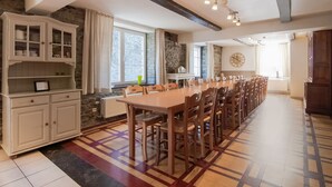 A spacious kitchen with a long wooden table, white cabinets, and a stone wall. - Timeless Cottage in Vresse-sur-semois With Terrace (Vresse-sur-Semois)