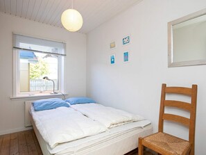 A bedroom with a bed, a wooden chair, a window with blinds, and wall art.