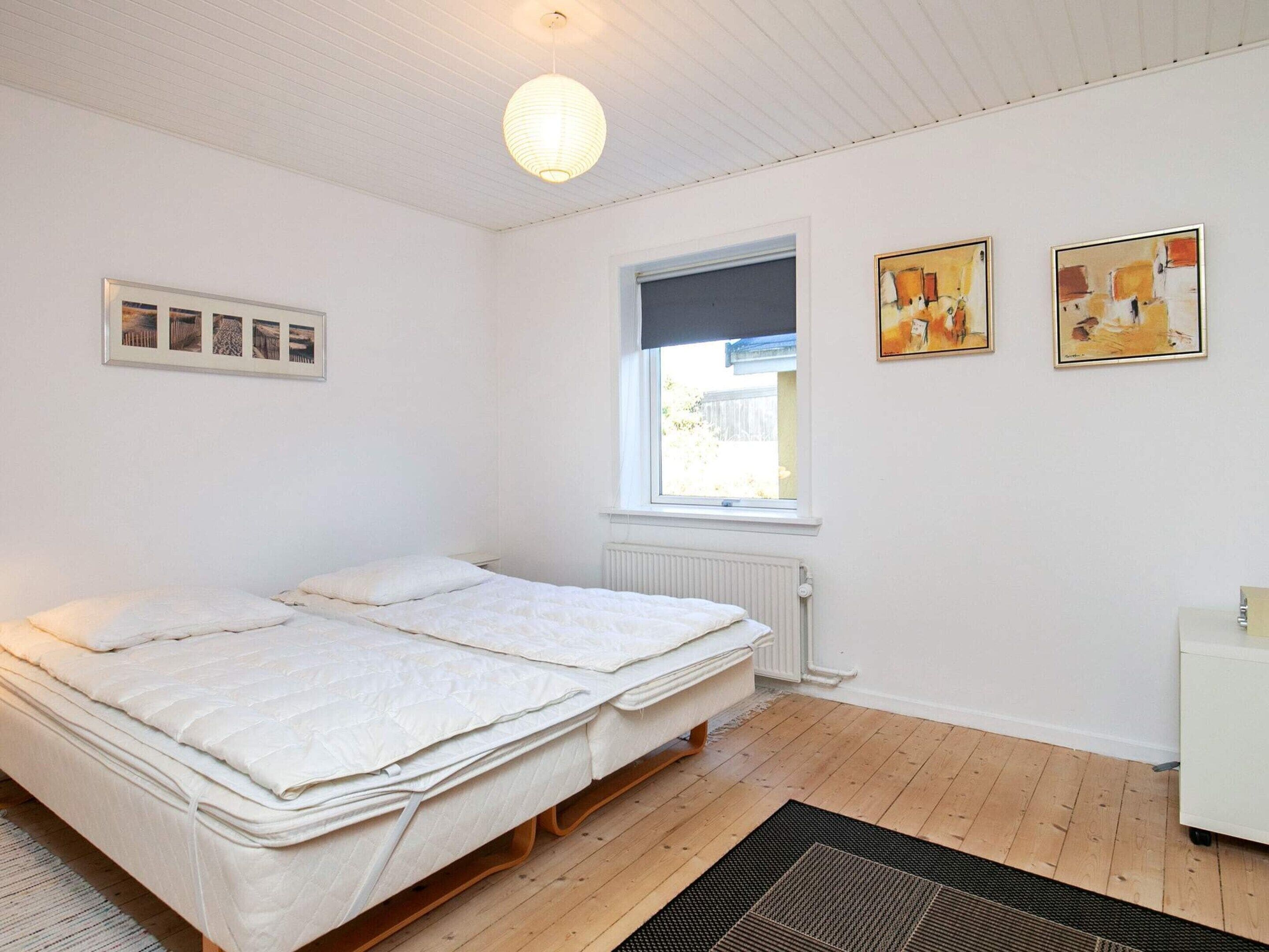 A bedroom with a bed, a window, and two paintings on the wall.
