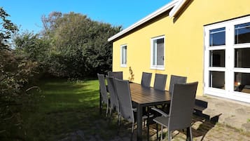 A yellow building with a patio table and chairs, surrounded by a grassy area and trees.