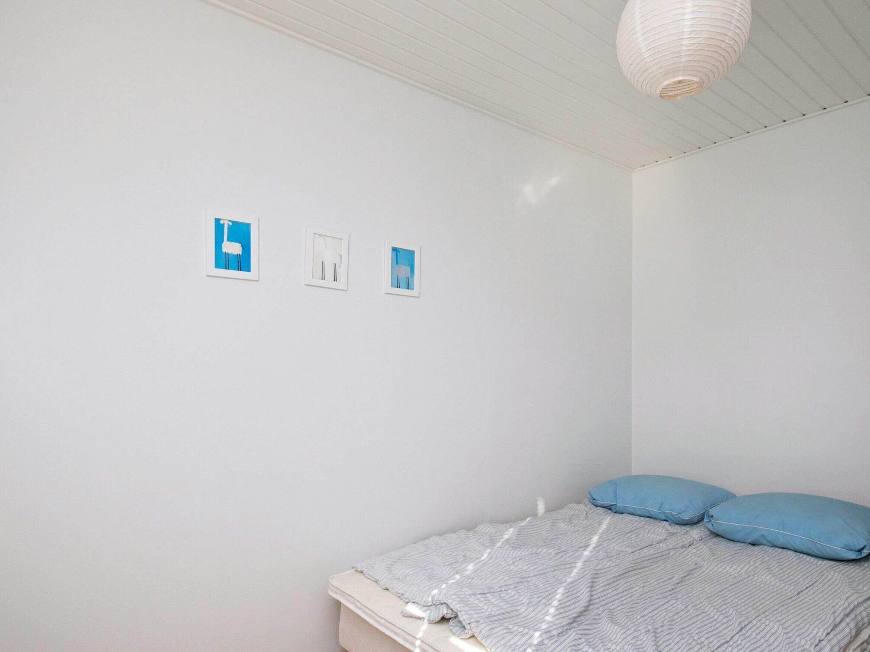 A bedroom with a bed, pillows, and three framed pictures on the wall.