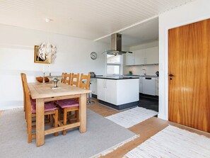 Et moderne køkken med hvide skabe, et træspisebord og et ur på væggen.