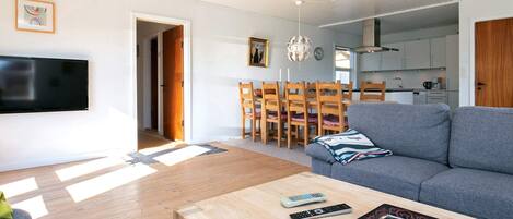 Ein modernes Wohnzimmer mit grauem Sofa, einem Holzesstisch und einem an der Wand befestigten Fernseher.