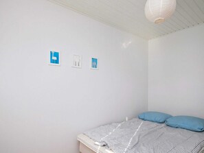 Simple, serene bedroom with a single bed, framed artwork, and a pendant light.