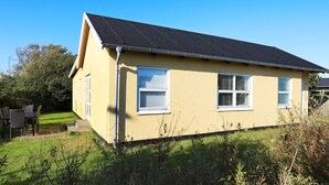 A single-story house with a dark roof, light yellow exterior walls, and white-framed windows.